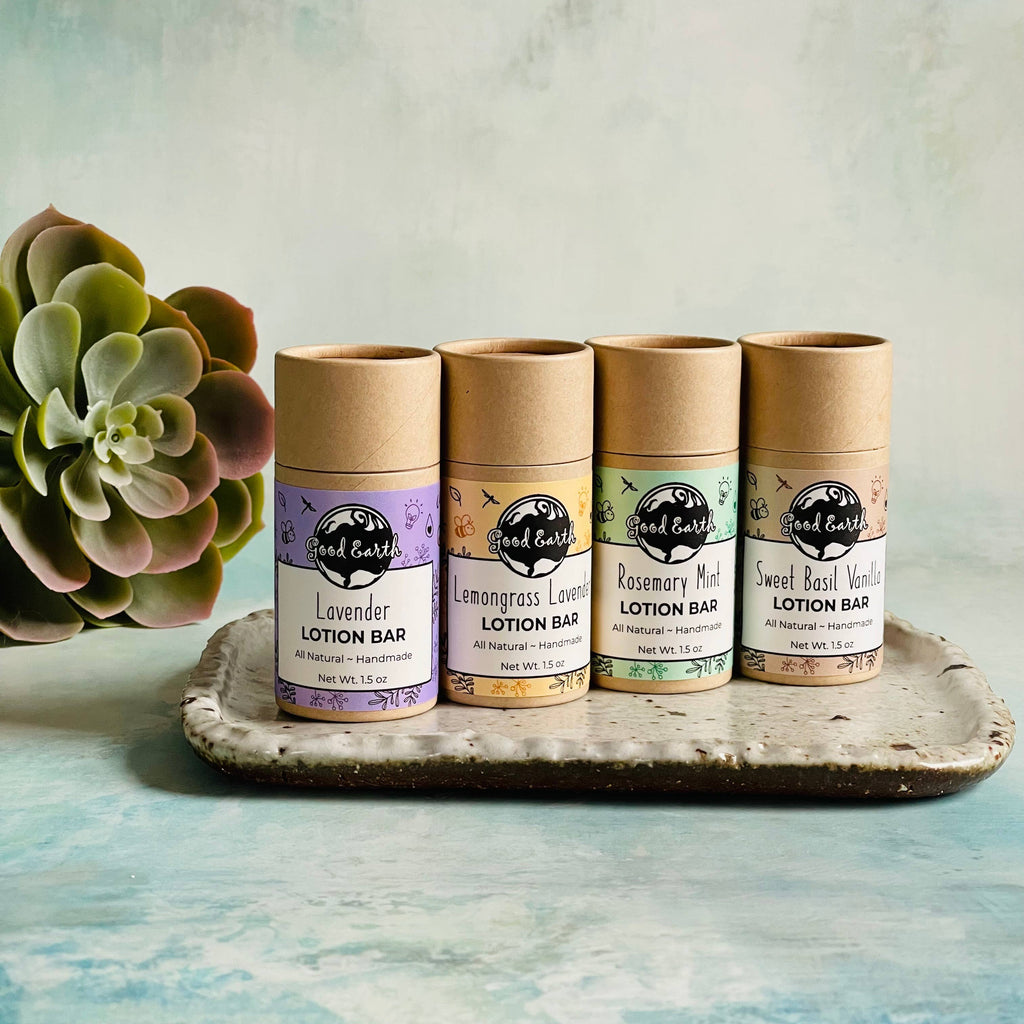 A selection of four lotion bars in cardboard tubes, each with a different essential oil scent, displayed in a line on a ceramic dish with a succulent plant to the side.