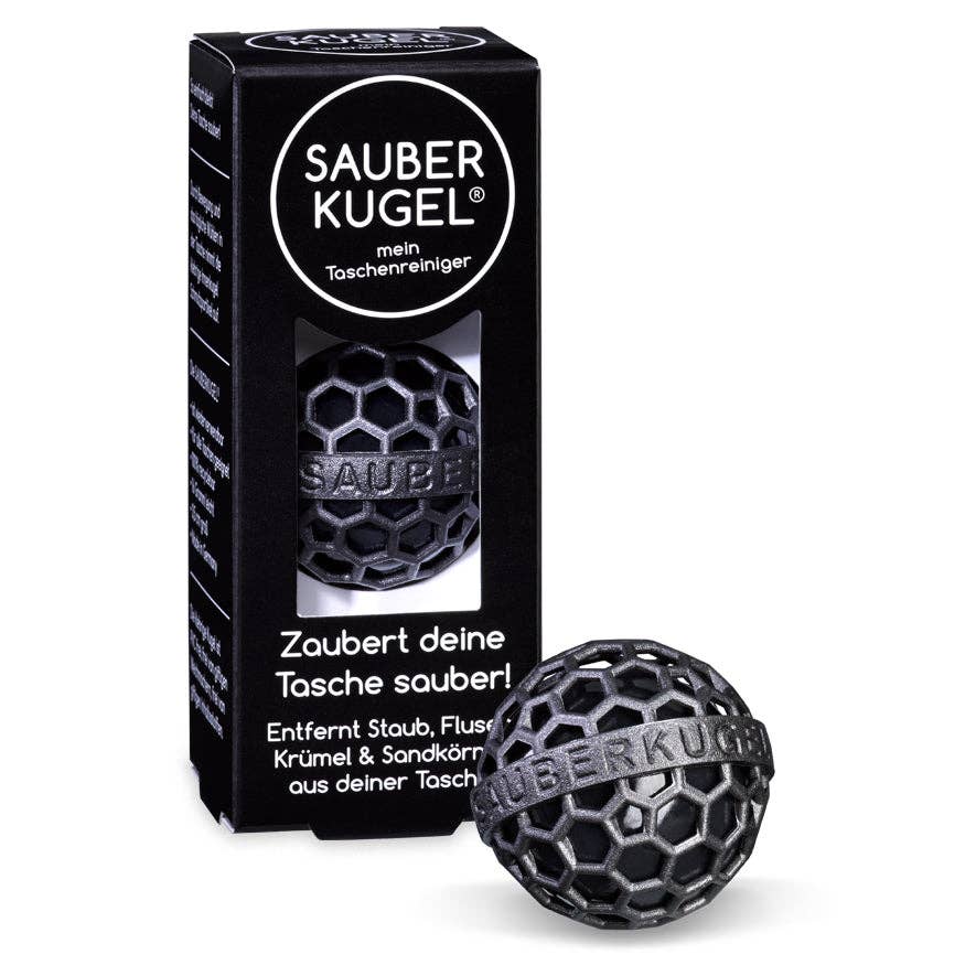 A black packaging box with the product name 'SAUBER KUGEL' and a visible black sticky cleaning ball, designed to remove dust and debris from bags.