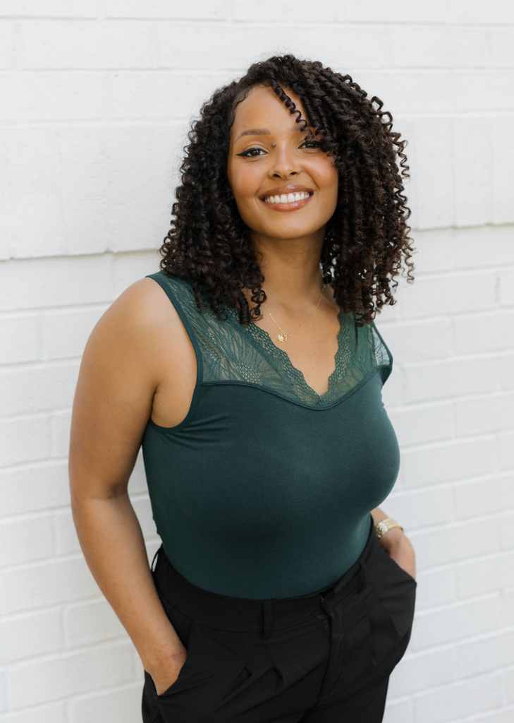 Woman wearing a green top with lace detail against a white brick wall