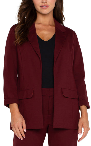 A woman modeling a bordeaux blazer with princess dart styling, two front flap pockets, and a relaxed fit.