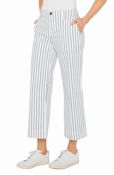 A pair of cropped, wide leg indigo stripe crop pants with front and back pockets, worn by a model with hands in pockets, paired with white sneakers.