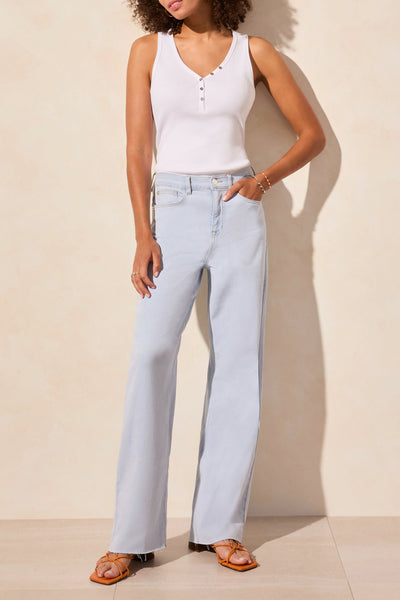A woman standing in a casual pose wearing a white top and light wash blue jeans with a high-rise waist and wide leg.