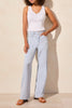 A woman standing in a casual pose wearing a white top and light wash blue jeans with a high-rise waist and wide leg.