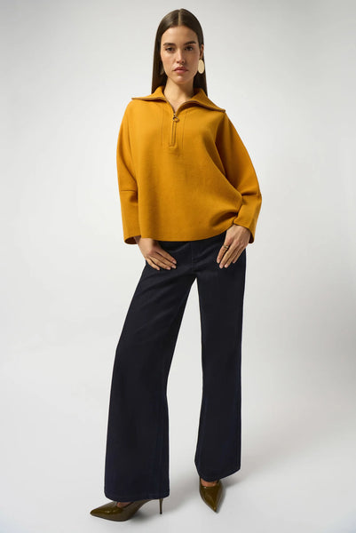 Woman wearing a mustard yellow sweater and black pants on a white background