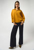 Woman wearing a mustard yellow sweater and black pants on a white background
