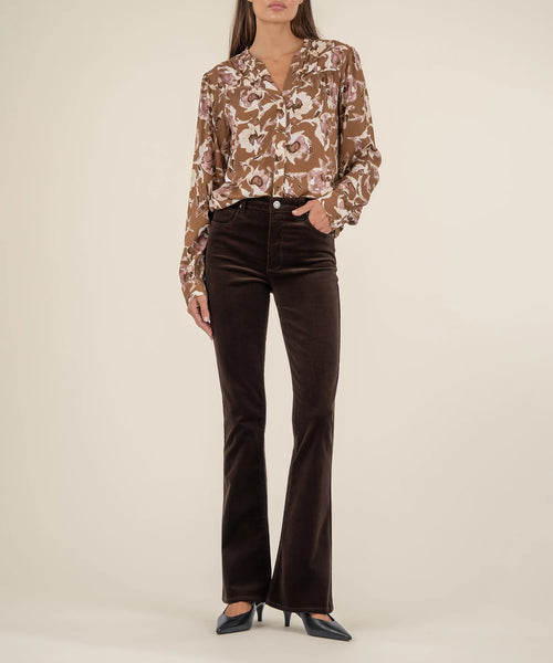 Woman wearing a patterned blouse and brown velvet pants on a beige background