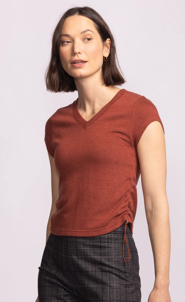 Woman wearing a rust-colored sleeveless top with a plain background