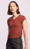 Woman wearing a rust-colored sleeveless top with a plain background