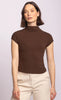 Woman wearing a brown turtleneck top and beige pants against a light purple background