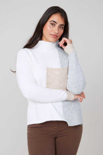 Woman wearing a white and gray sweater with a neutral color block design on a plain background