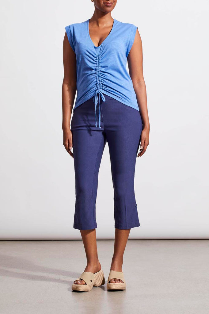 A person wearing a blue sleeveless top with a neckline, paired with navy capri pants. Accessory sandals are visible.