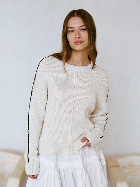 Woman wearing a cream sweater with black trim against a plain background