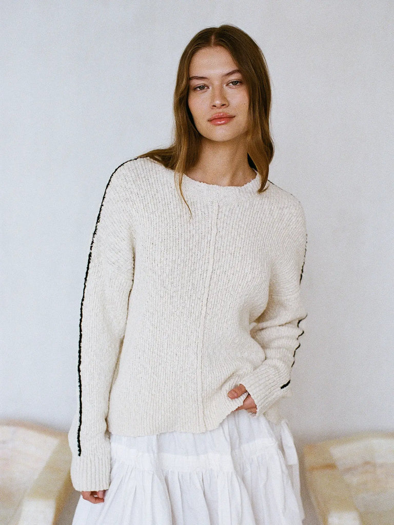 Woman wearing a cream sweater with black trim against a plain background