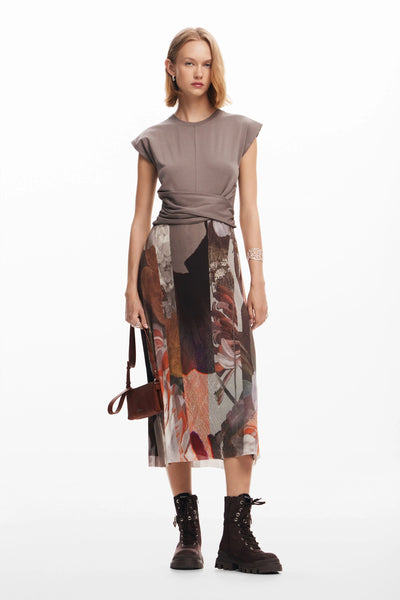 A female model wearing a gray Tierra dress with short sleeves and a knee-length skirt with a floral pattern. She is also wearing black boots and carrying a brown bag.