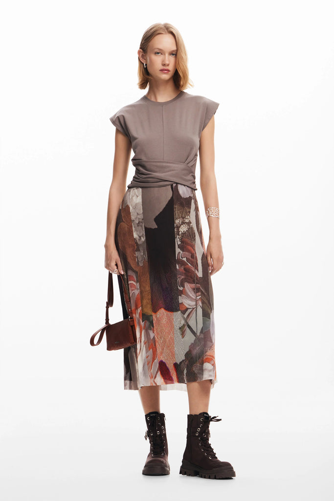 A female model wearing a gray Tierra dress with short sleeves and a knee-length skirt with a floral pattern. She is also wearing black boots and carrying a brown bag.