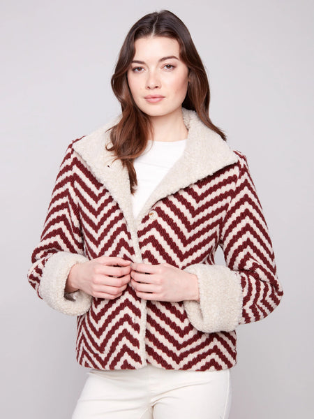 Woman wearing a red and white chevron pattern jacket with a fur-lined collar on a light gray background