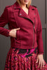 A person wearing a red suede biker jacket with a round neckline and zipper details, paired with a multicolored skirt.