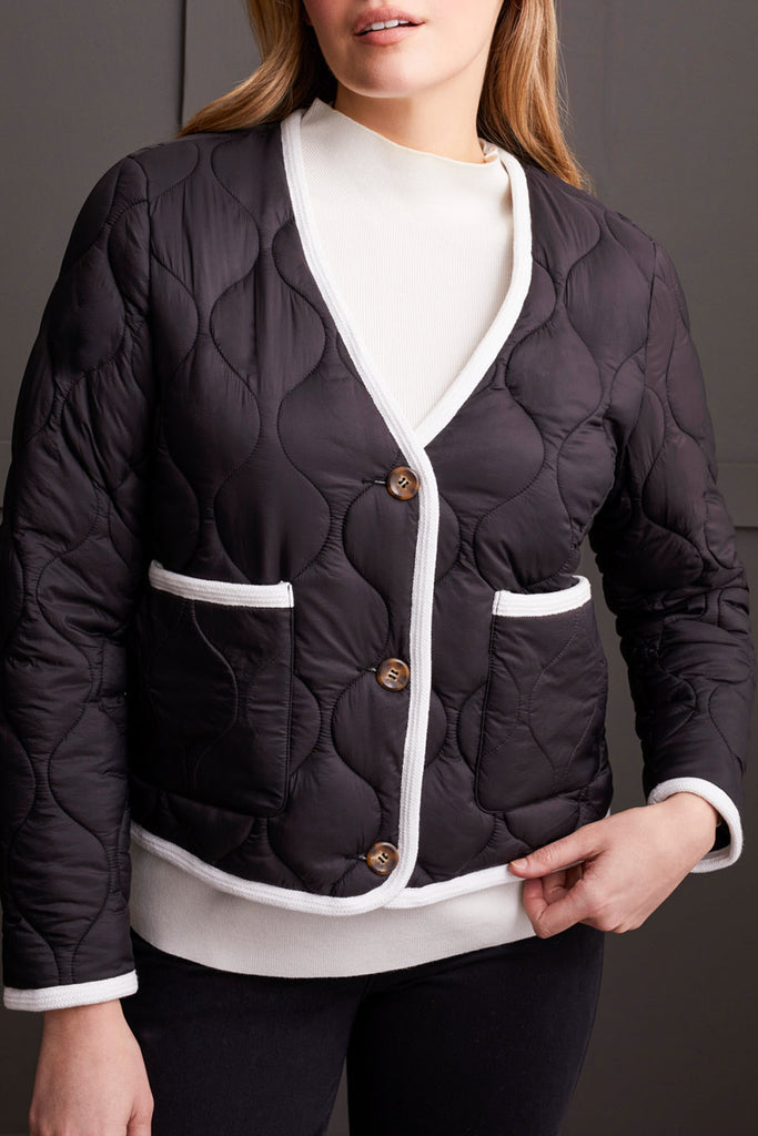 A woman wearing a black button front puffer jacket with white quilting and white button details, paired with a white top and black trousers.